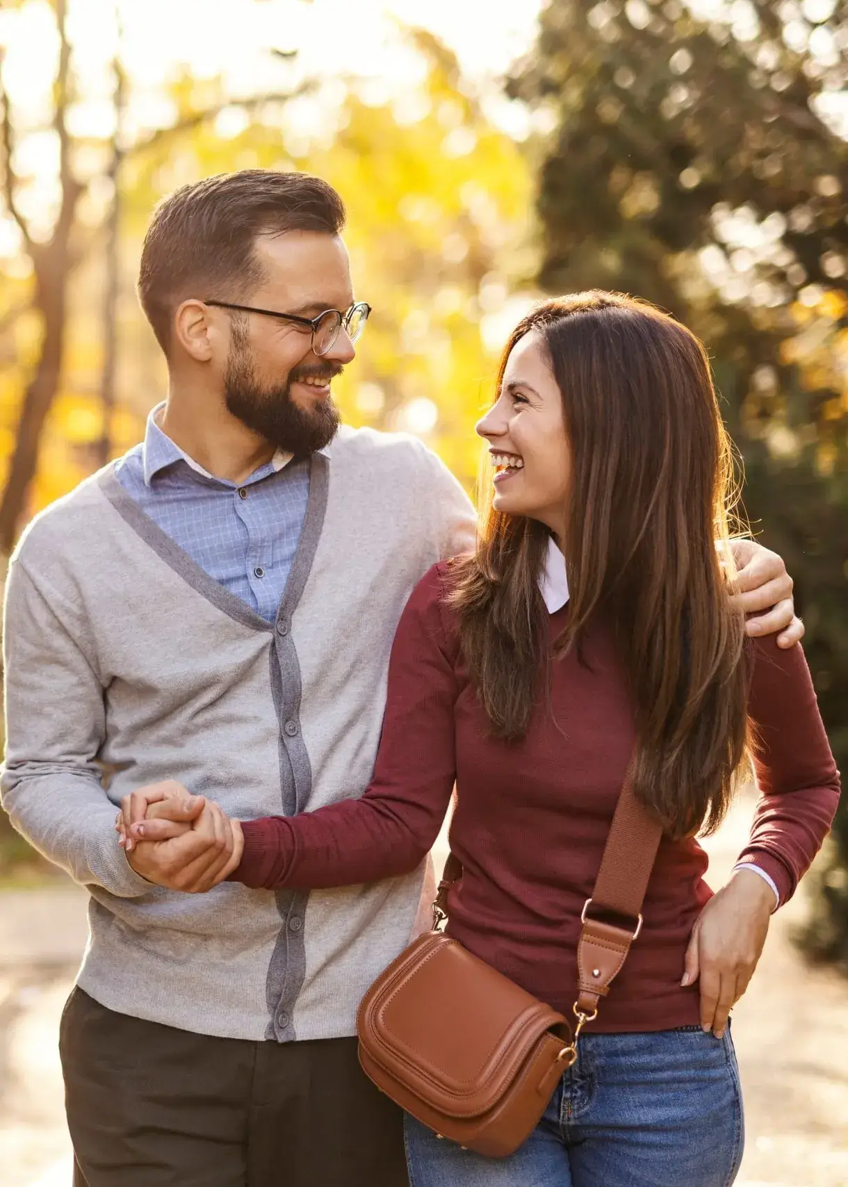Smiling couple walking arm in arm along a sunlit autumn path
